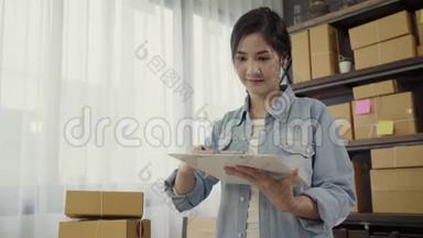 美丽聪明的亚洲青年企业家女企业家中小企业检查产品库存和写在剪贴板上工作。